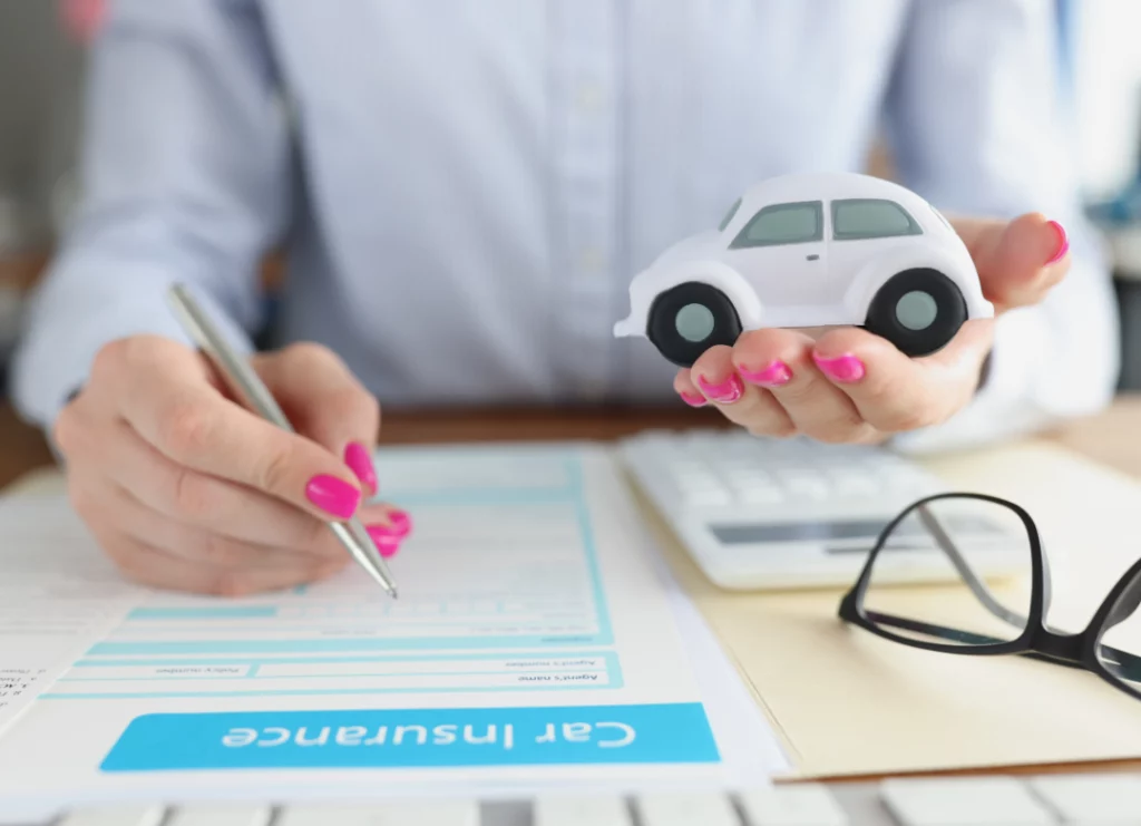 A person filling out a car insurance form and holding a white toy car in one hand.